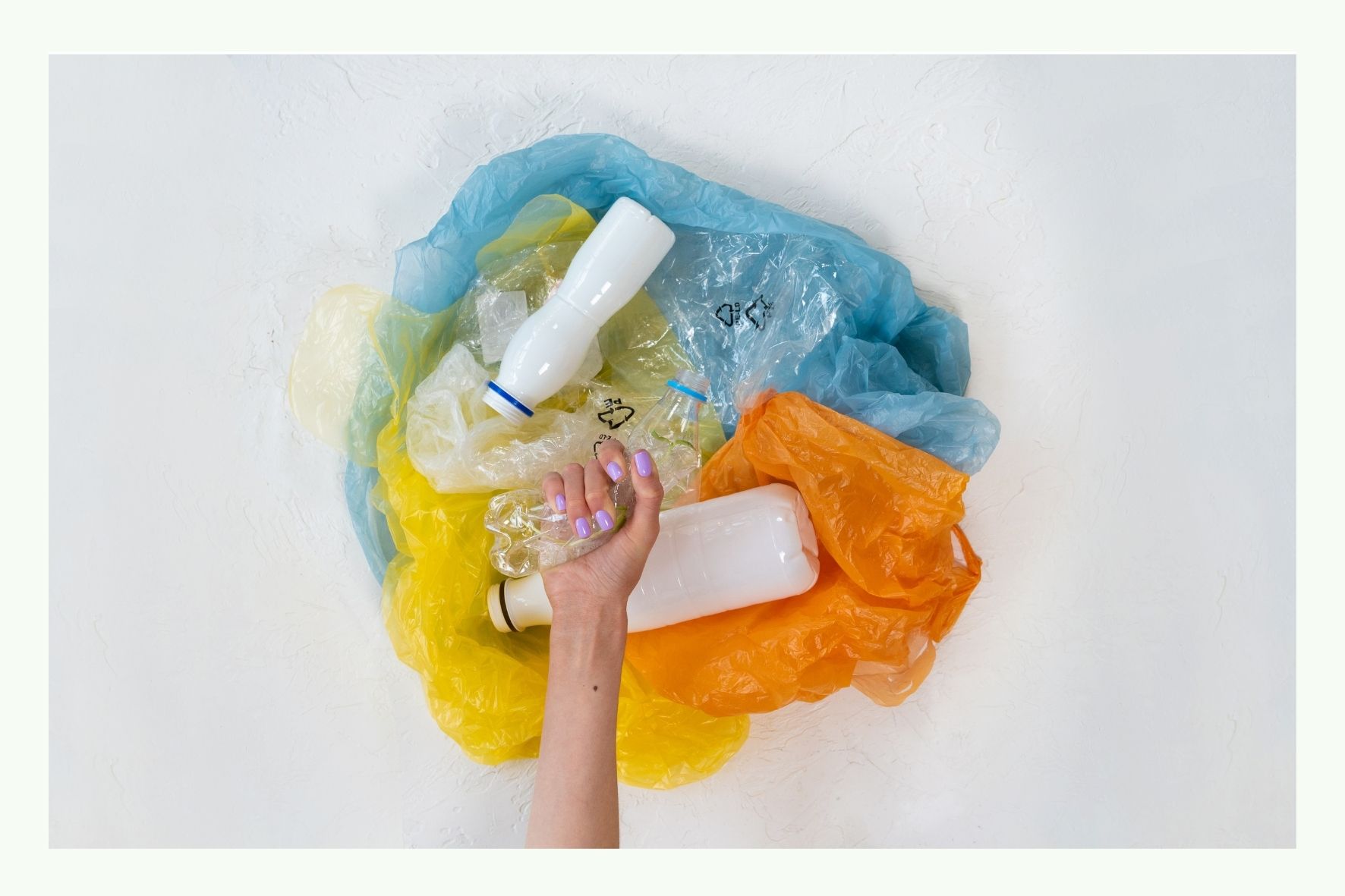 Mano che tiene una bottiglia bianca tra pellicole di plastica colorate Mano che tiene una bottiglia bianca tra pellicole di plastica colorate