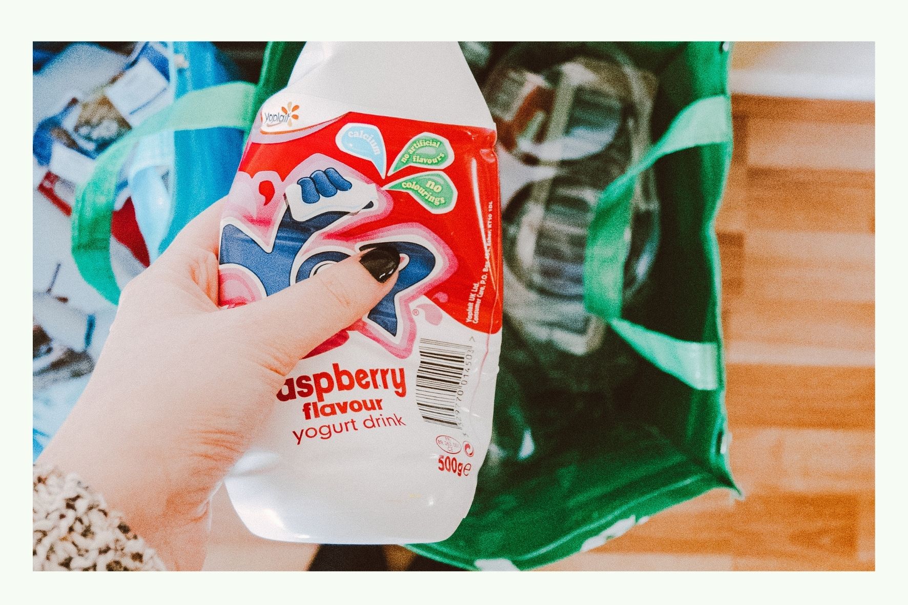 Hand hält einen leeren Kunststoff-Joghurtbehälter über einer grünen Recyclingtasche Hand hält einen leeren Kunststoff-Joghurtbehälter über einer grünen Recyclingtasche