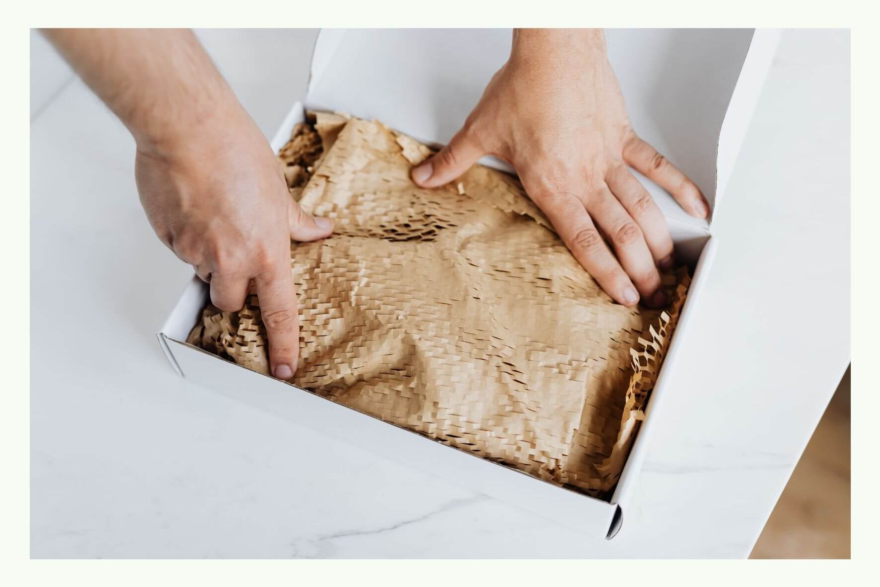 Hände legen Papierpolsterung in einen offenen Versandkarton