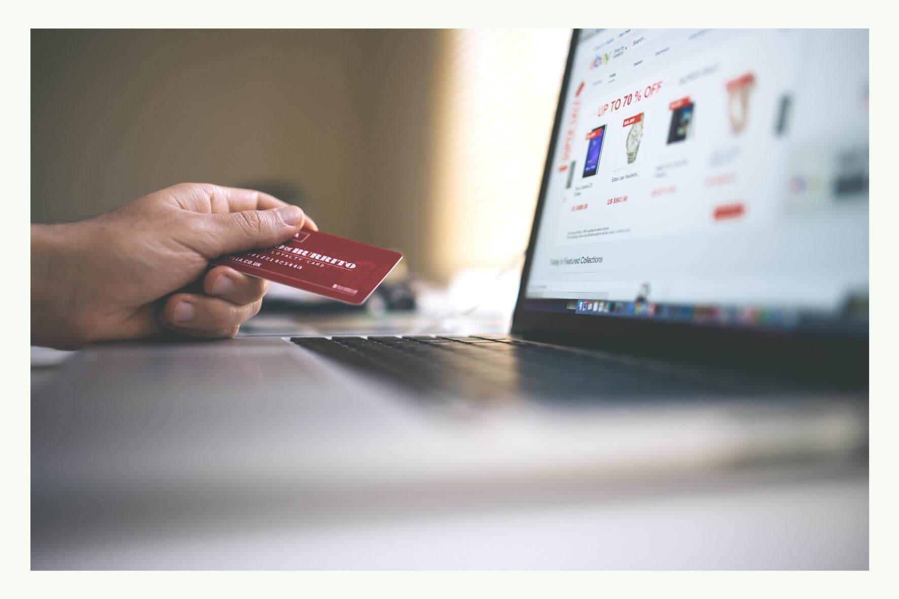 Hand holding a credit card in front of a laptop with an online shop page