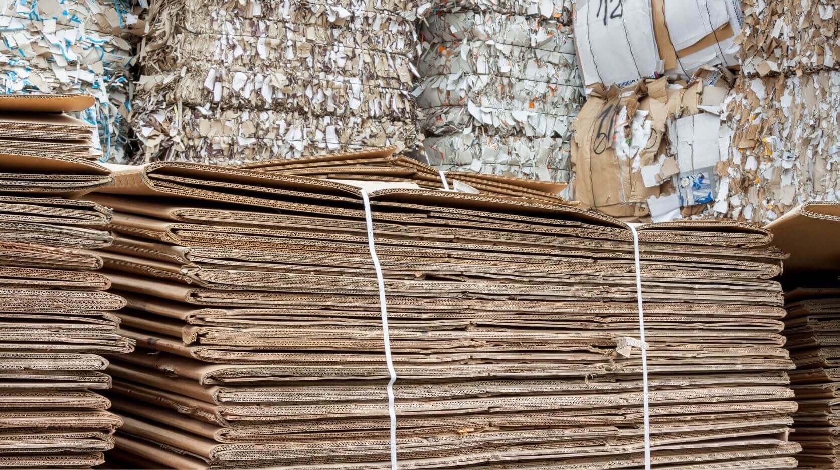 Gestapelte Wellpappkartons vor Ballen aus gepresstem Altpapier Gestapelte Wellpappkartons vor Ballen aus gepresstem Altpapier