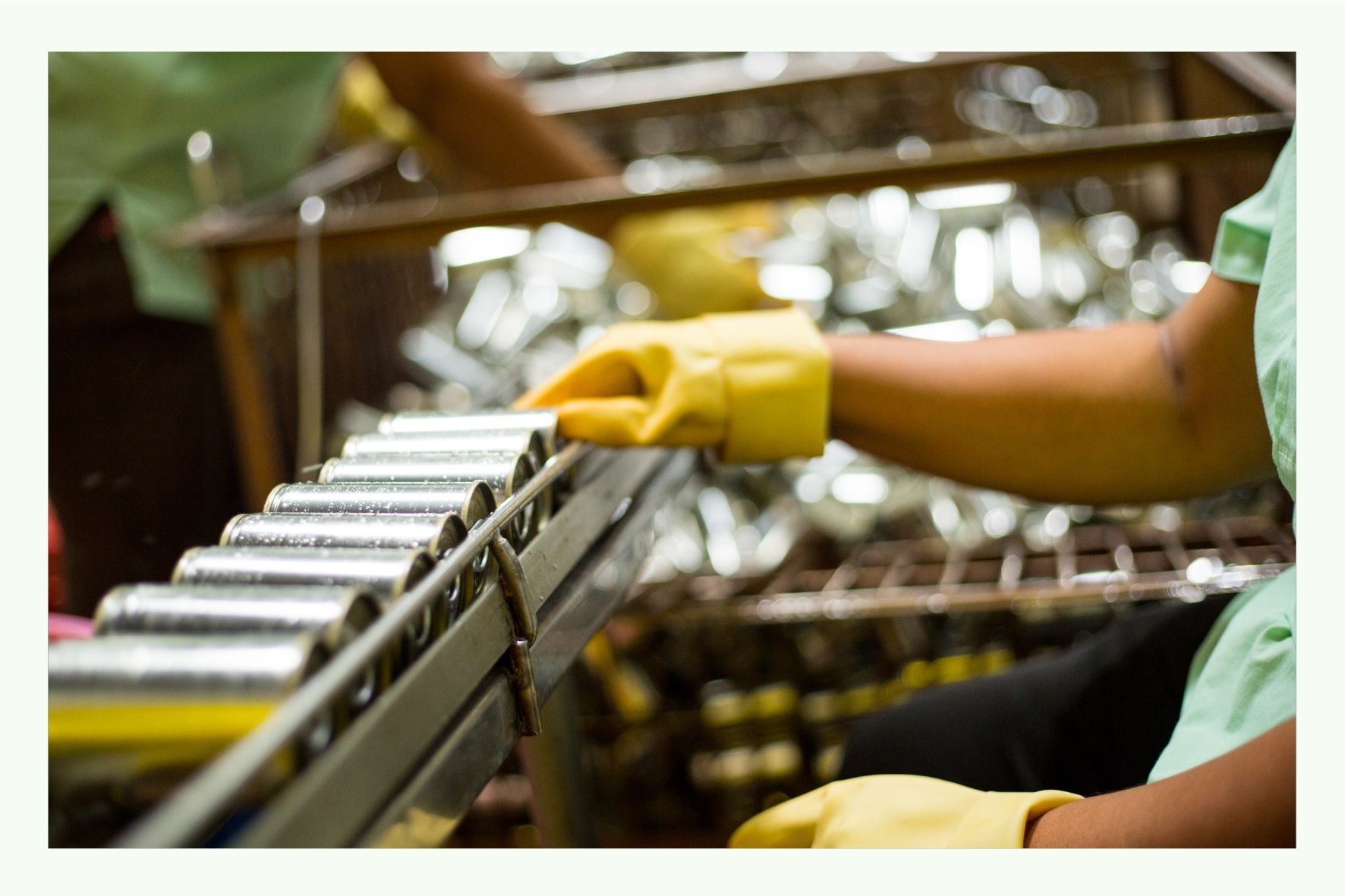 Workers with yellow gloves sorting metal parts on a conveyor belt